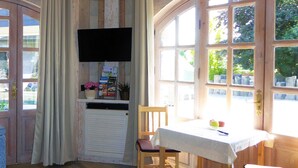 Une pièce comprenant une table et des chaises, un téléviseur fixé au mur et une fenêtre donnant sur un paysage verdoyant.