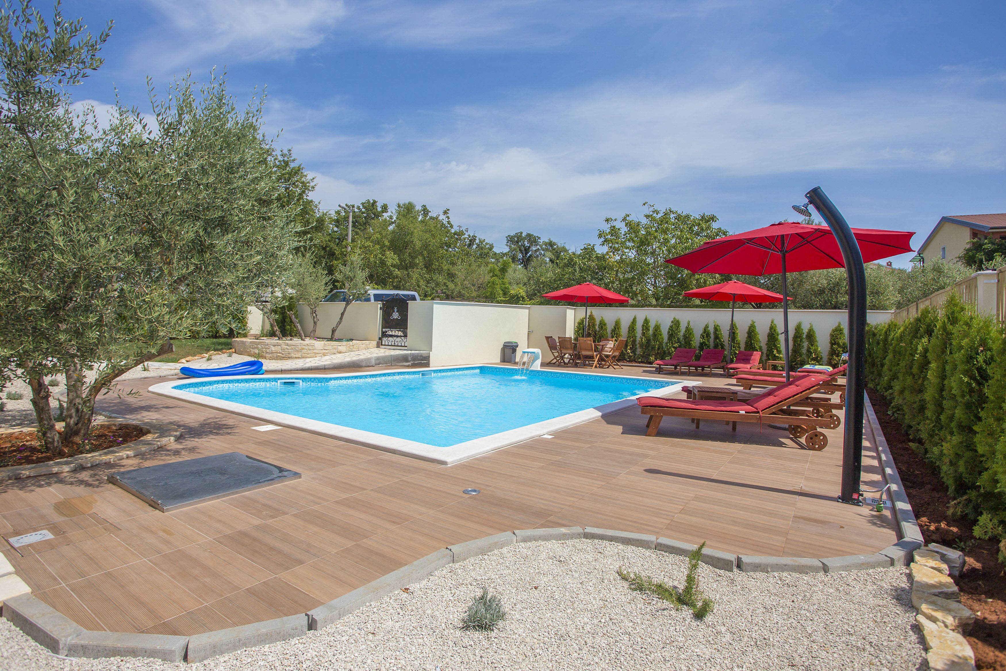 A swimming pool with a wooden deck, red umbrellas, and lounge chairs.