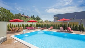 Piscina com espreguiçadeiras e guarda-sóis vermelhos, cercada por um deck de madeira e uma cerca de bambu.