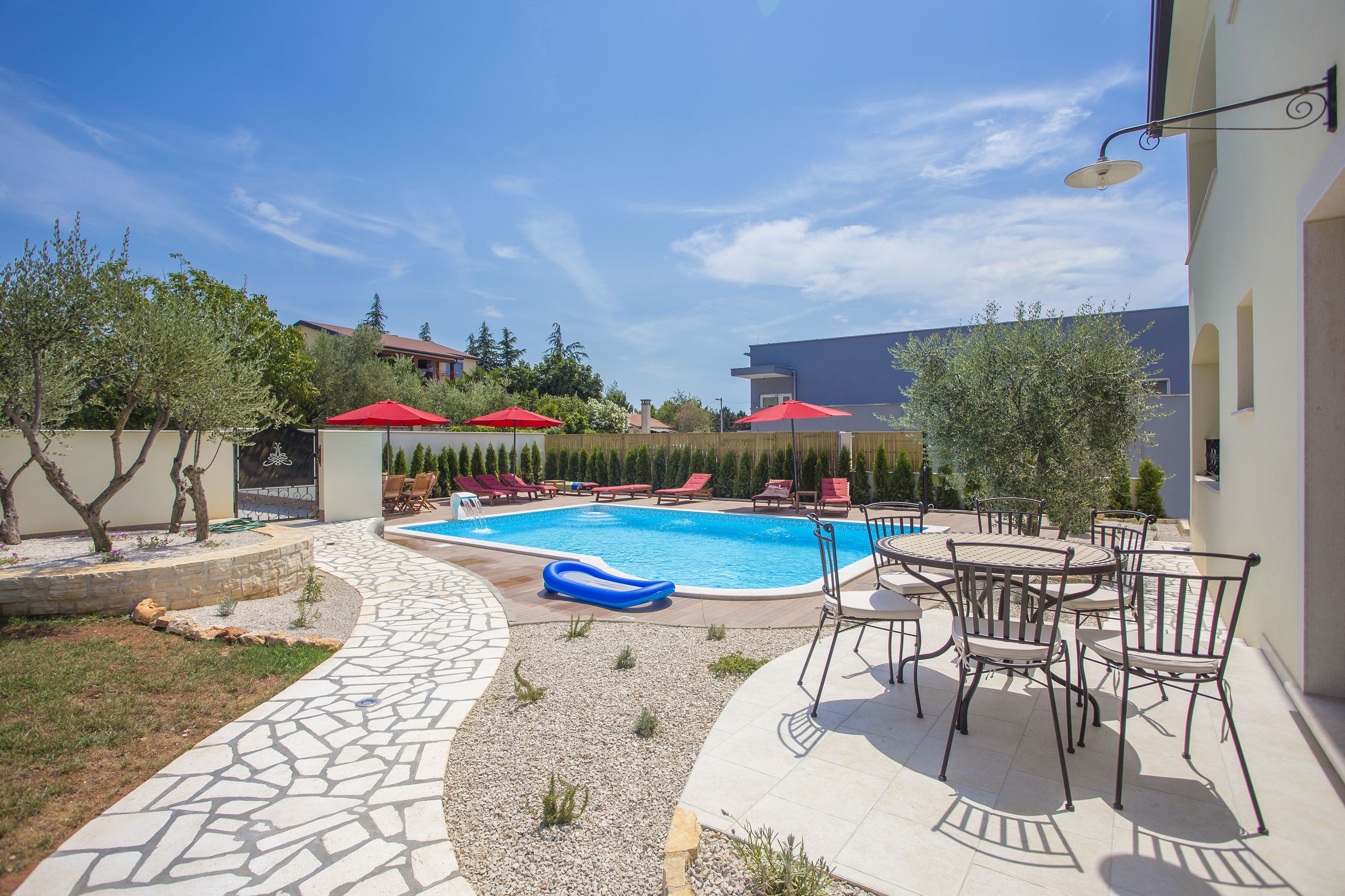 A swimming pool with lounge chairs and umbrellas, surrounded by a stone patio and greenery.