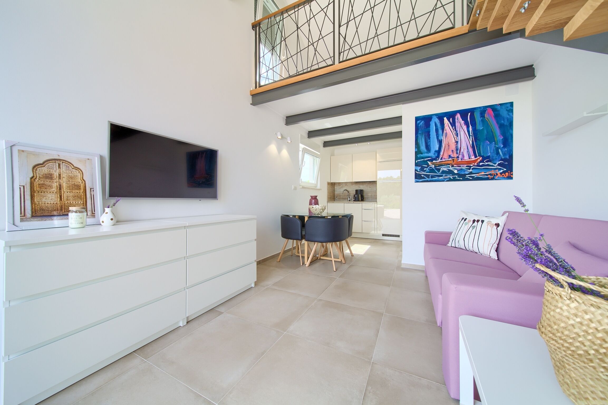 A modern living room with a white console, a purple sofa, a dining area with two chairs, and a kitchen in the background.