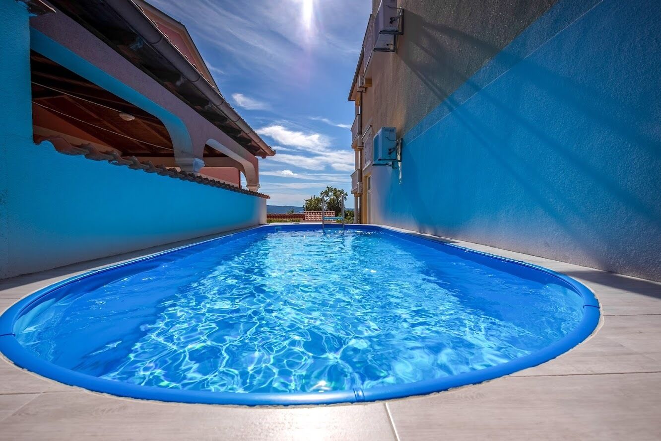 Une piscine à l’eau d’un bleu cristallin, entourée de bâtiments aux murs bleus et au sol carrelé.