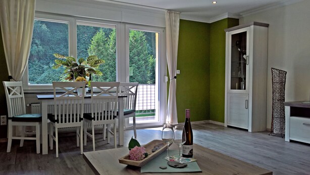 A dining area with a table and chairs, a bottle of wine, and a vase of flowers. - (g) Roosike vacation in Bacharach-Steeg, modern apartment in the countryside (Bacharach)