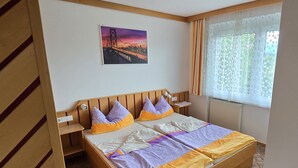 A bedroom with a wooden headboard, a bed with a purple and yellow striped blanket, a pillow, and a window with curtains.