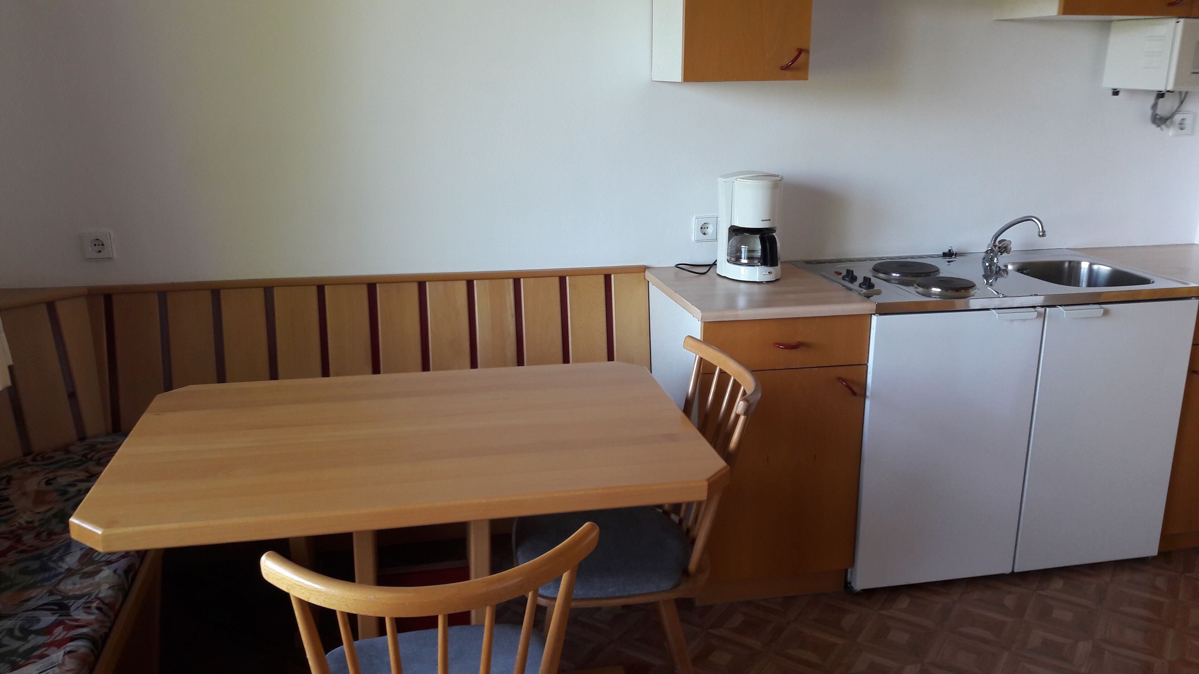 Une cuisine compacte avec une table et des chaises en bois, une machine à café, un évier et un réfrigérateur.