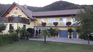 A yellow two-story house with a sloped roof, a balcony with hanging flower baskets, and a garage door.