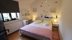 A bedroom with a bed, bedside tables, a window with plants, and wall decorations. - Peaceful Haven - 3BR/1BA Apt, Sleeps 5, Parking 1 (Banjole)