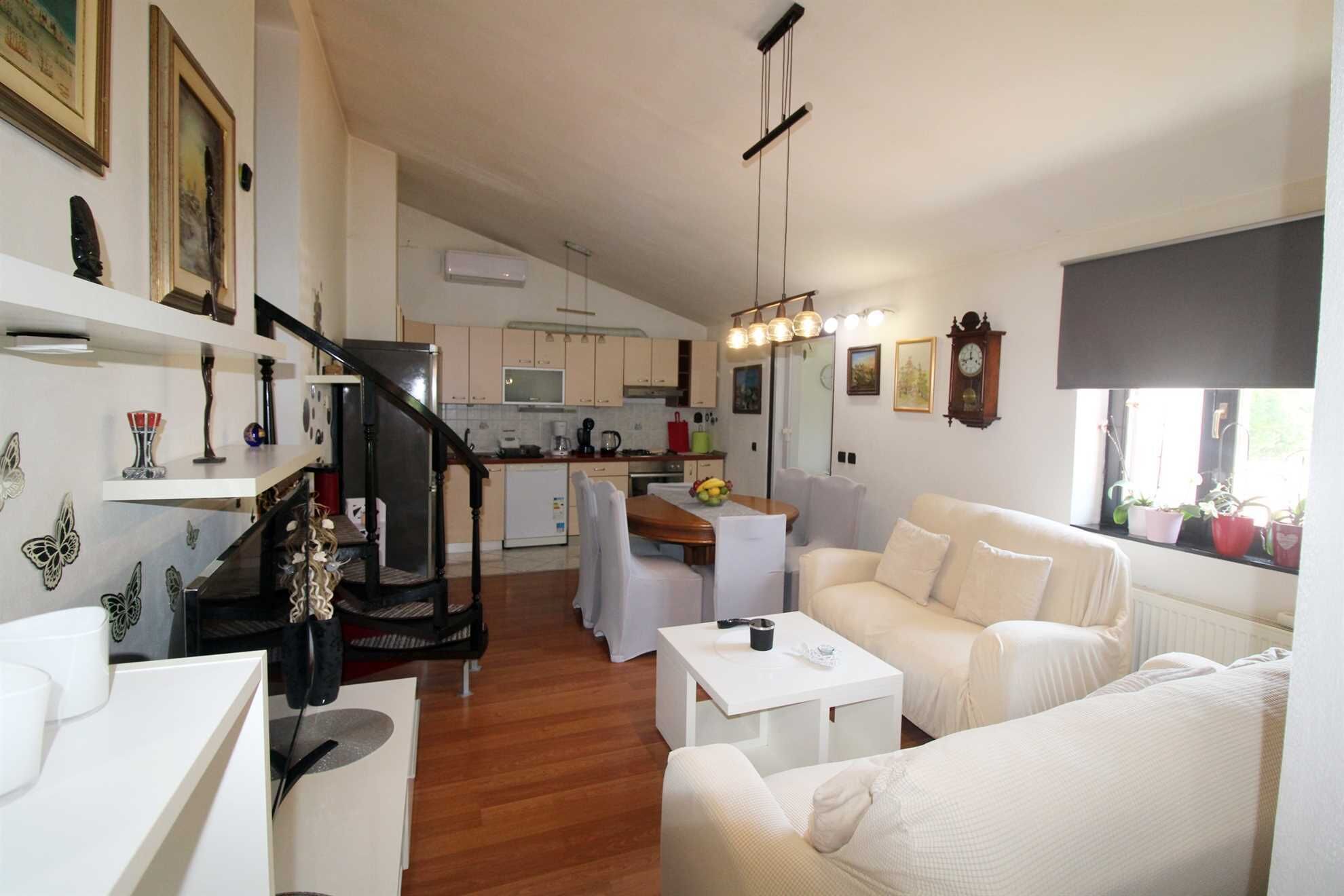 A modern living room with a staircase, a dining area, and a kitchen.