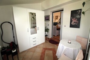 Un espace de vie compact comprenant une armoire blanche, une petite table à manger, un aspirateur et une plante en pot.