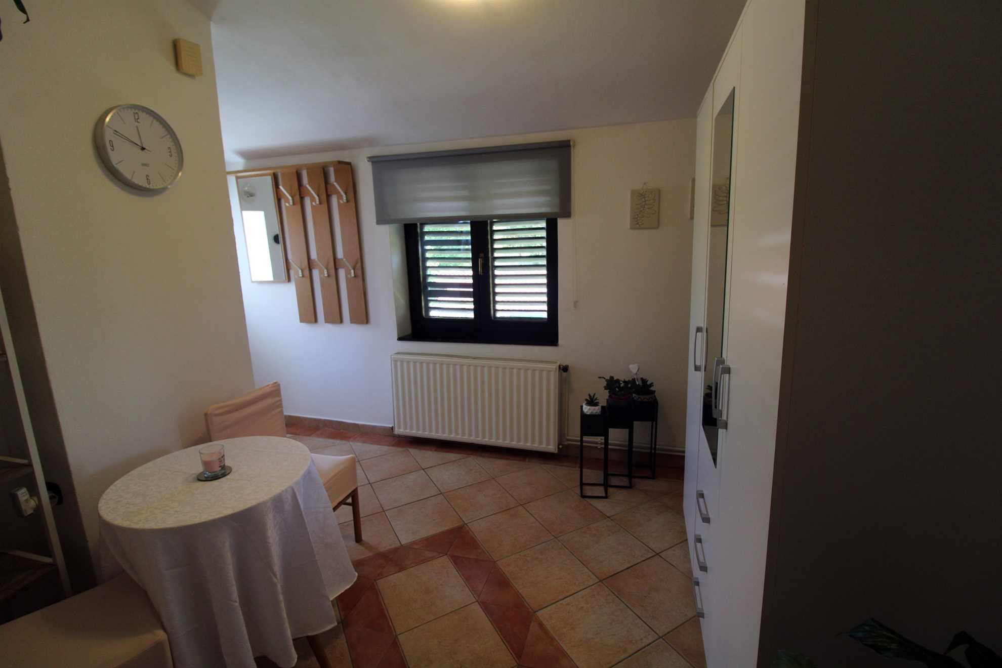 Une petite pièce bien éclairée, avec une table ronde, des chaises, un radiateur et une fenêtre avec des stores.
