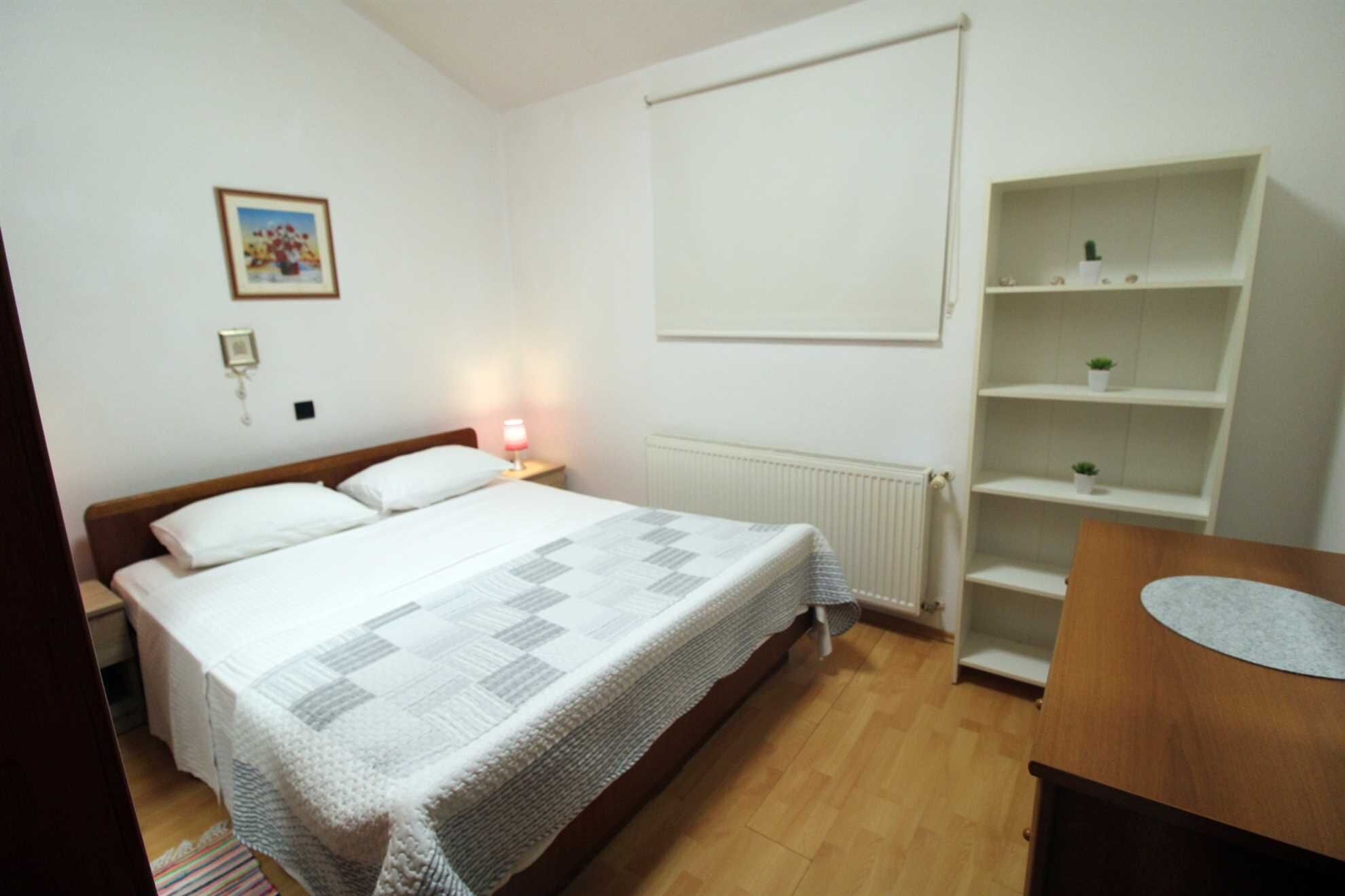 Ein Schlafzimmer mit Bett, Nachttischlampe, weißen Wänden, einer Heizung und einem Holznachttisch.