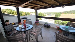 A covered outdoor patio with a round table and chairs, potted plants, and a grill. - Peaceful Haven - 3BR/1BA Apt, Sleeps 5, Parking 1 (Banjole)