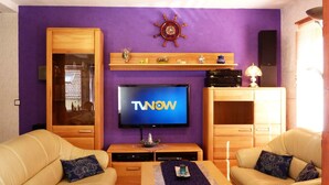 A living room with a TV, two sofas, a wooden cabinet, and a shelf with decorative items. - Pure relaxation with steam shower and whirlpool in a comfort cottage  (Bad Berleburg)