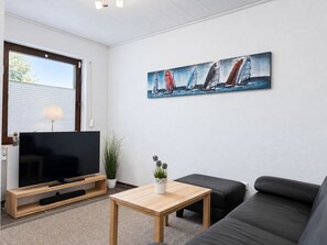 A modern living room with a flat-screen TV, a wooden coffee table, a black leather sofa, and a painting of sailboats on the wall.