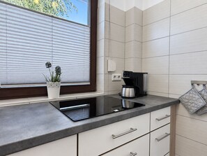 A modern kitchen with a built-in stove, a coffee maker, and a potted plant on the windowsill.
