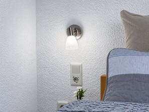 A bedroom with a bed, a wall-mounted light fixture, and a power outlet.