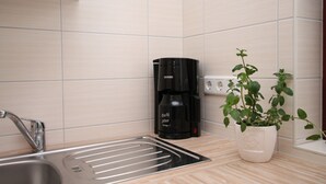 Eine Küche mit Spüle aus Edelstahl, einer schwarzen Kaffeemaschine und einem Topf mit Pflanze.