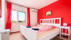 Une chambre avec un lit blanc, des rideaux rouges, une fenêtre donnant sur un beau paysage et une petite table de chevet blanche avec une lampe.