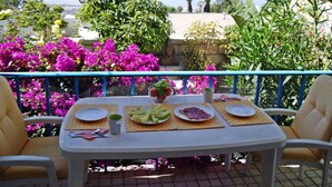 Une table dressée à l’extérieur, avec des assiettes, des couverts et une carafe, entourée de fleurs et de verdure aux couleurs vives.