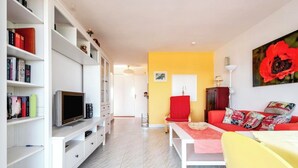 Un salon moderne avec un téléviseur, des étagères, un canapé rouge et un mur d’accent jaune.