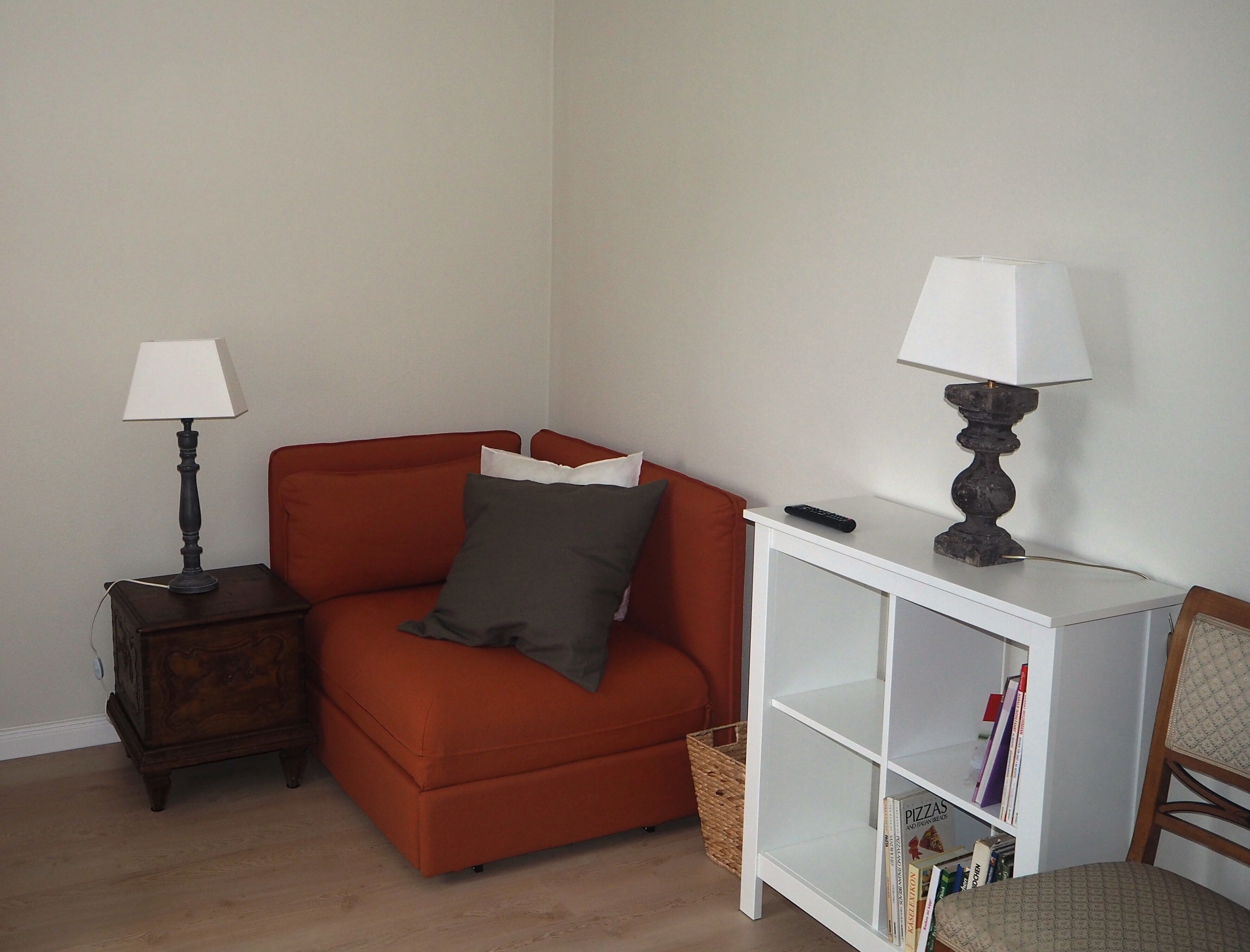 Una sala de estar con un sofá, dos lámparas, una mesita auxiliar, una estantería y una silla.