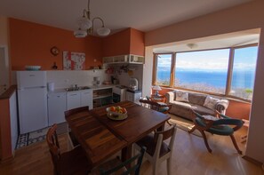 Une cuisine avec une table et des chaises, une vue sur la mer grâce à de grandes fenêtres, et un canapé dans l’espace salon.