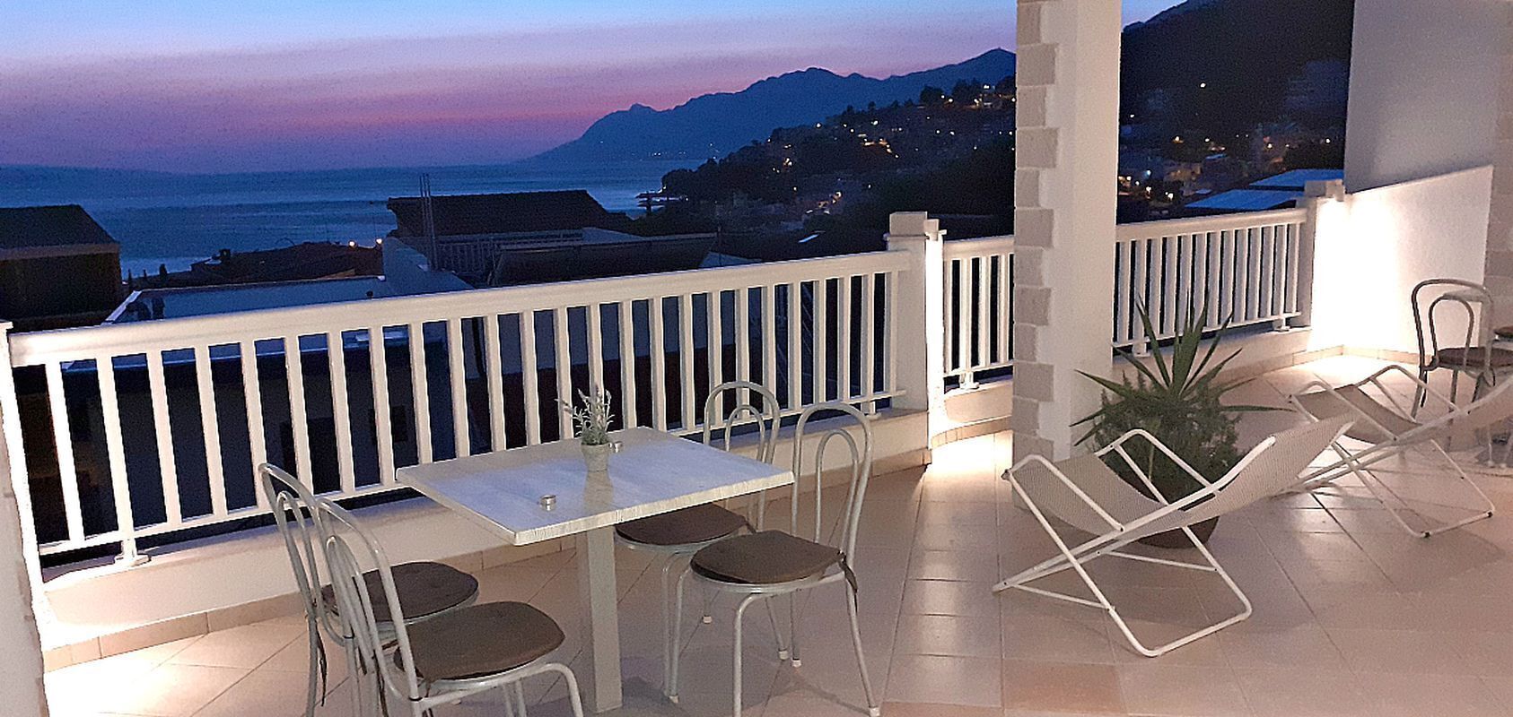 Ein Balkon mit Tisch und Stühlen, mit Blick auf die Küste, Berge und eine Stadt in der Ferne.