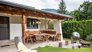 An outdoor patio with a wooden table and chairs, a barbecue grill, and a white furry chair. - SKI IN - SKI OUT at the Eichenhof ski lifts (St.Johann In Tirol)