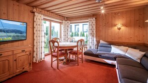 A wooden cabin interior with a dining table, chairs, a sofa, and a TV mounted on the wall. - SKI IN - SKI OUT at the Eichenhof ski lifts (St.Johann In Tirol)