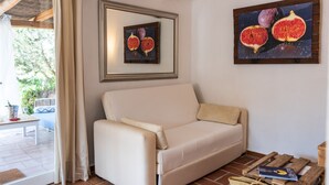 A living room with a beige sofa, a framed picture of figs, and a wooden coffee table with a book. - Tasteful house, 2 double rooms, 2 bathrooms, large terrace, garden with outdoor shower,  (Es Pujols)