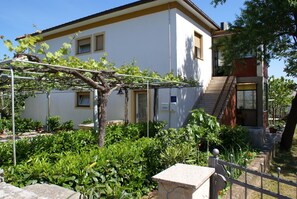 Stunning residential building with a glass door entrance and a charming porch area, surrounded by lush greenery and a pergola.