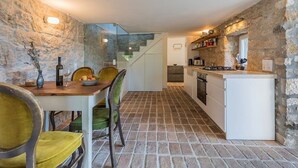 Une cuisine compacte avec un mur en pierre, un coin repas avec une table et des chaises, et un petit îlot central doté d’un réfrigérateur.