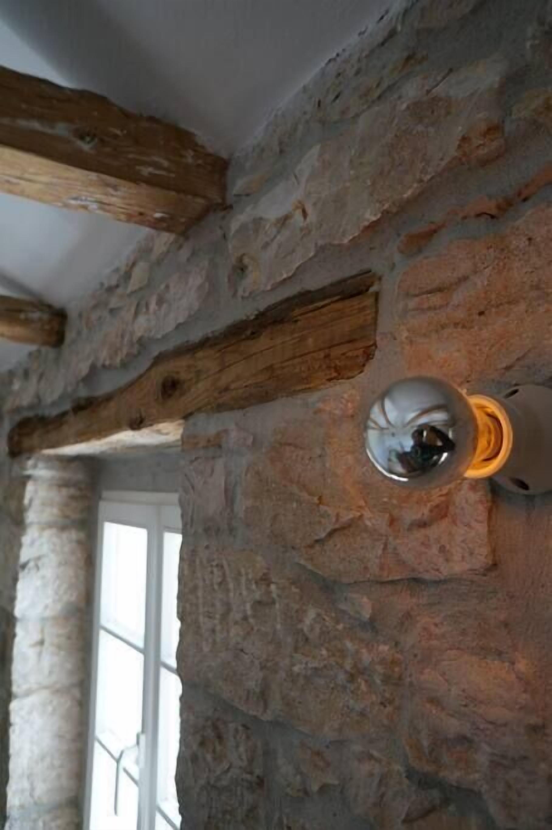 A stone wall with exposed wooden beams and a light fixture.