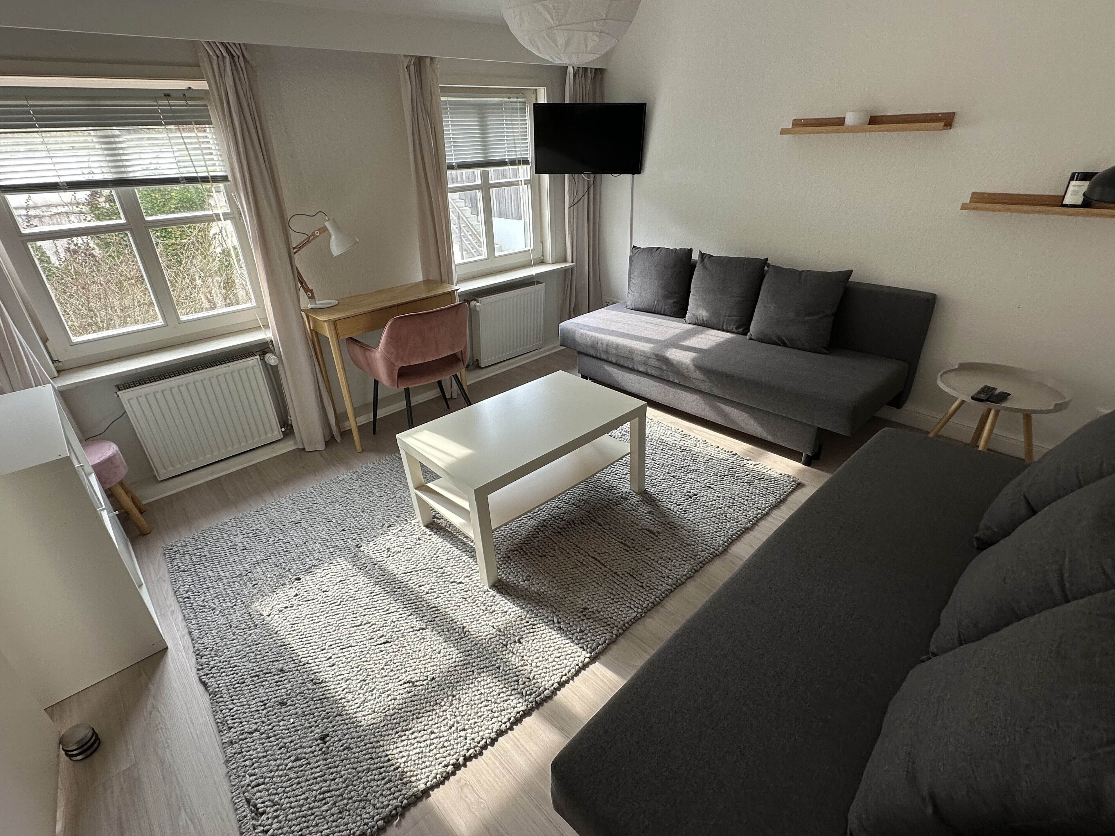 Ein modernes Wohnzimmer mit einem grauen Sofa, einem weißen Couchtisch, einem pinken Sessel und einem an der Wand befestigten Fernseher.