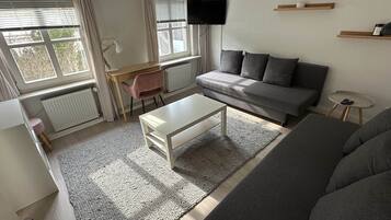 Ein modernes Wohnzimmer mit einem grauen Sofa, einem weißen Couchtisch, einem pinken Sessel und einem an der Wand befestigten Fernseher.