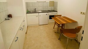 Una cuina compacta amb zona de menjador, armaris blancs, un refrigerador petit, una cuina i una làmpada penjant.