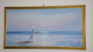 Una pintura d'una dona amb un vestit blanc al costat del mar, amb un marc daurat.