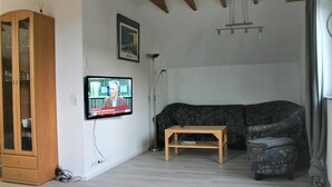 A living room with a wooden cabinet, a television mounted on the wall, a floor lamp, a sofa, and a small table. - Detached holiday home, apartment 1 / for 2-4 persons, W-LAn free (Mehren/Daun)