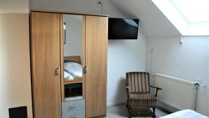 A bedroom with a wooden wardrobe, a single bed, a striped armchair, and a mounted TV. - Detached holiday home, apartment 1 / for 2-4 persons, W-LAn free (Mehren/Daun)