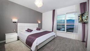 Ein modernes Schlafzimmer mit einem großen Bett, zwei Nachttischen, einem flauschigen Teppich und Meerblick durch ein großes Fenster.