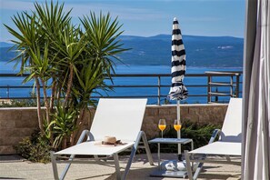 A terrace with two white lounge chairs, a striped umbrella, and a table with two glasses of orange juice. - Villa Red with pool, seaview (Makarska)