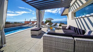 Ein Poolbereich auf dem Dach mit Liegestühlen, einer überdachten Sitzecke und Blick aufs Meer.
