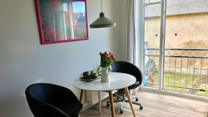 Une pièce moderne avec une table ronde, deux chaises noires, un vase blanc orné de fleurs rouges et un tableau accroché au mur.