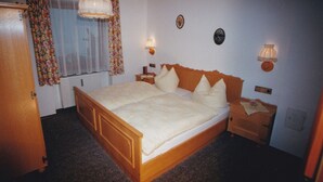 Une chambre à coucher avec un lit en bois, deux tables de chevet, une fenêtre ornée de rideaux à motifs floraux et des lampes fixées au mur.