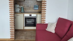 Un espace de vie compact comprenant un coin cuisine équipé d’une cuisinière, d’un four et d’une machine à café.