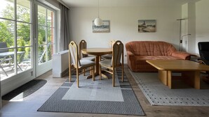 Moderni olohuone, jossa on suuri ikkuna, ruskea sohva, puinen sohvapöytä ja ruokapöytä tuoleineen.