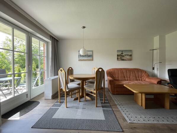 A modern living room with a large window, a brown sofa, a wooden coffee table, and a dining table with chairs.