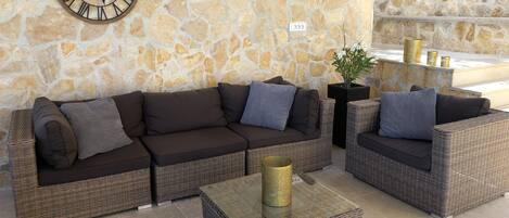 A stone wall with a clock, a brown sofa set, and wicker furniture.