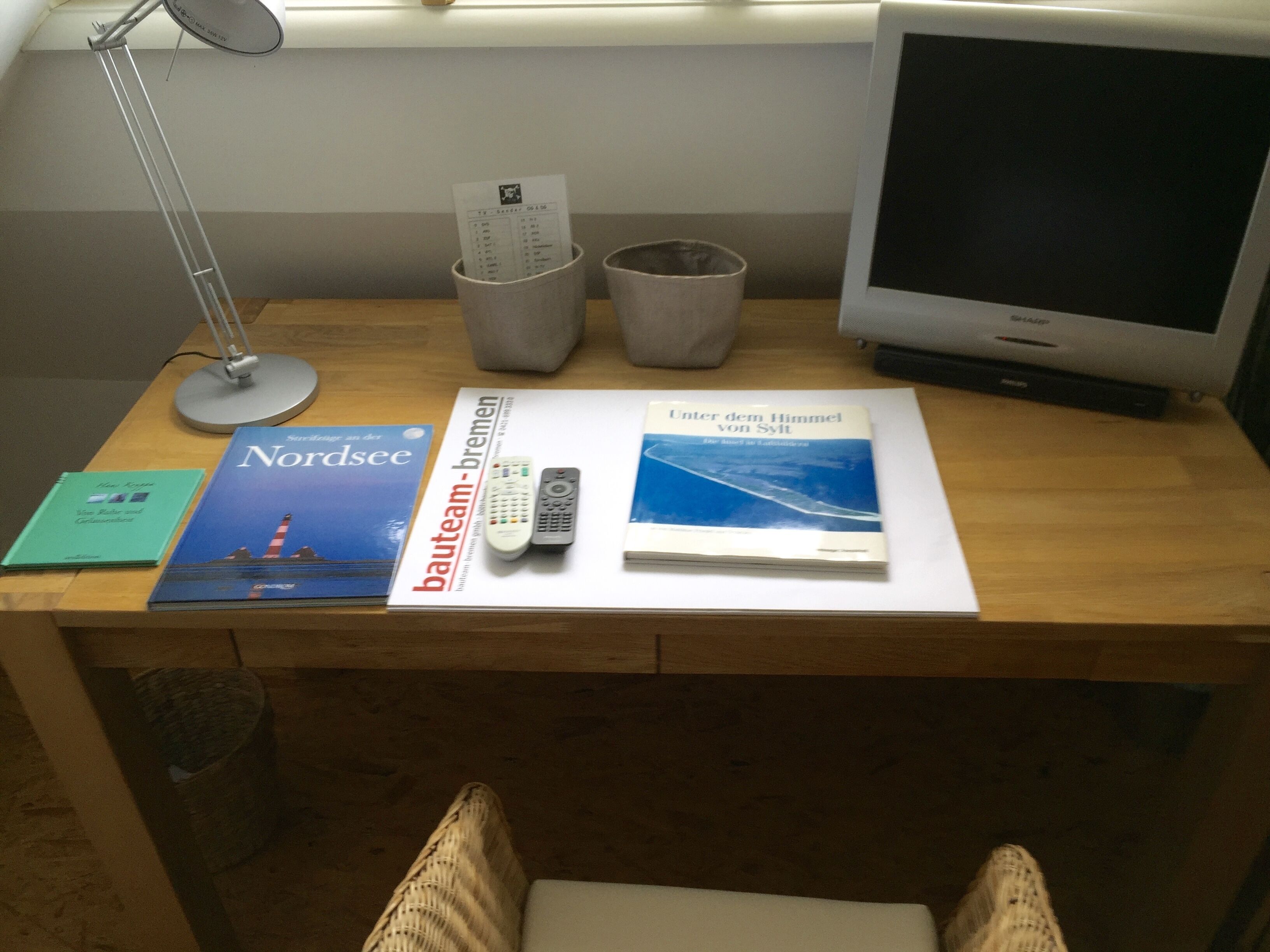 A desk with a lamp, remote controls, and books.