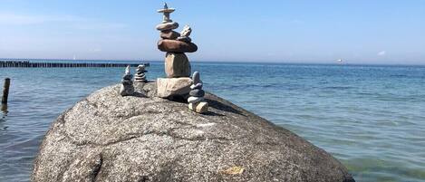 Un grand rocher surmonté d’un tas de pierres, dominant une mer calme sous un ciel dégagé.